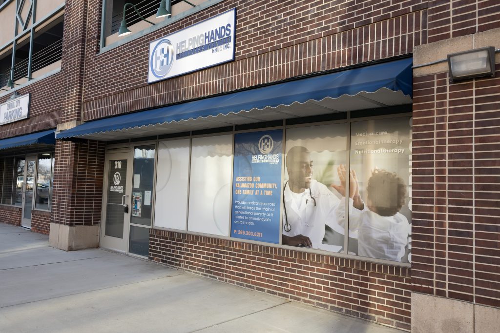 A brick building with a "Helping Hands" sign and a window graphic of a doctor and child high-fiving.
