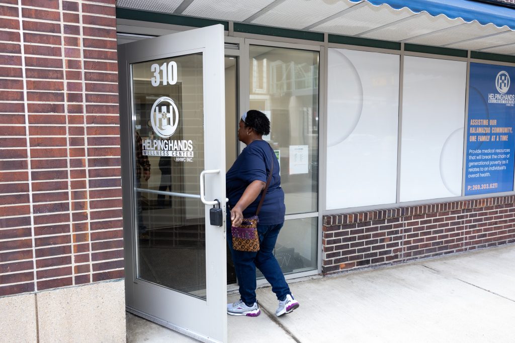 A person enters the Helping Hands Services Center through a glass door on a city sidewalk.